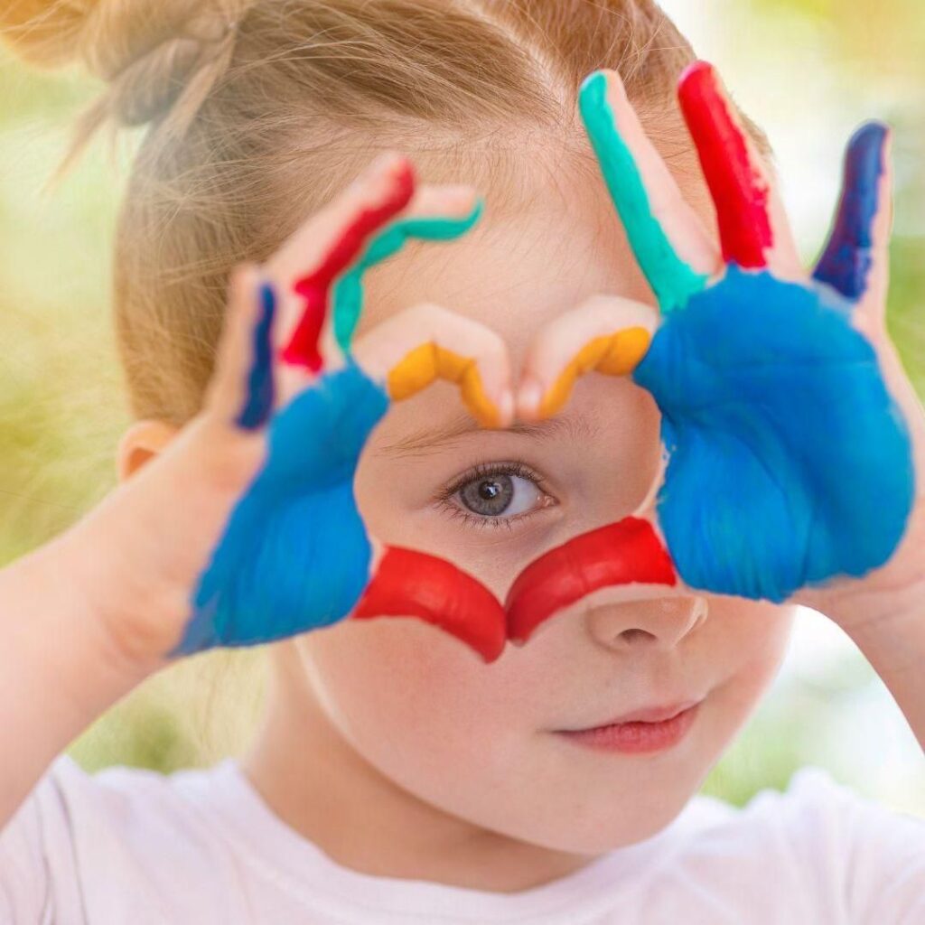 Niño jugando con pintura de colores y formando unos lentes con las manos, representando la psicología infantil y la expresión creativa.